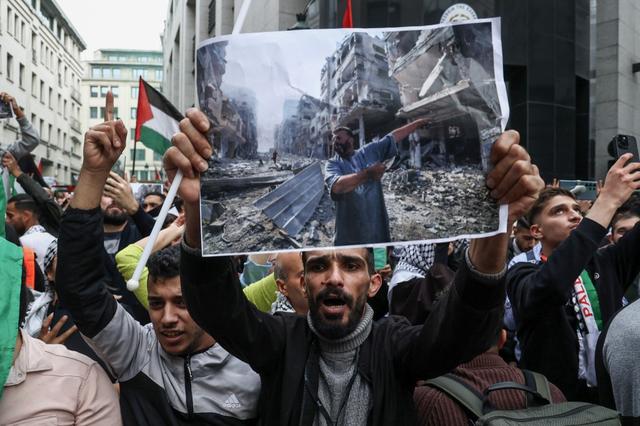 Un manifestant brandit une photo prise par Mahmud Hams – des personnes inspectant les dégâts suite à une attaque aérienne israélienne dans la bande de Gaza – lors d'une manifestation contre les opérations militaires d'Israël à Gaza et en soutien aux Palestinien.nes, à Bruxelles, le 11 octobre 2023. [AFP - KENZO TRIBOUILLARD]