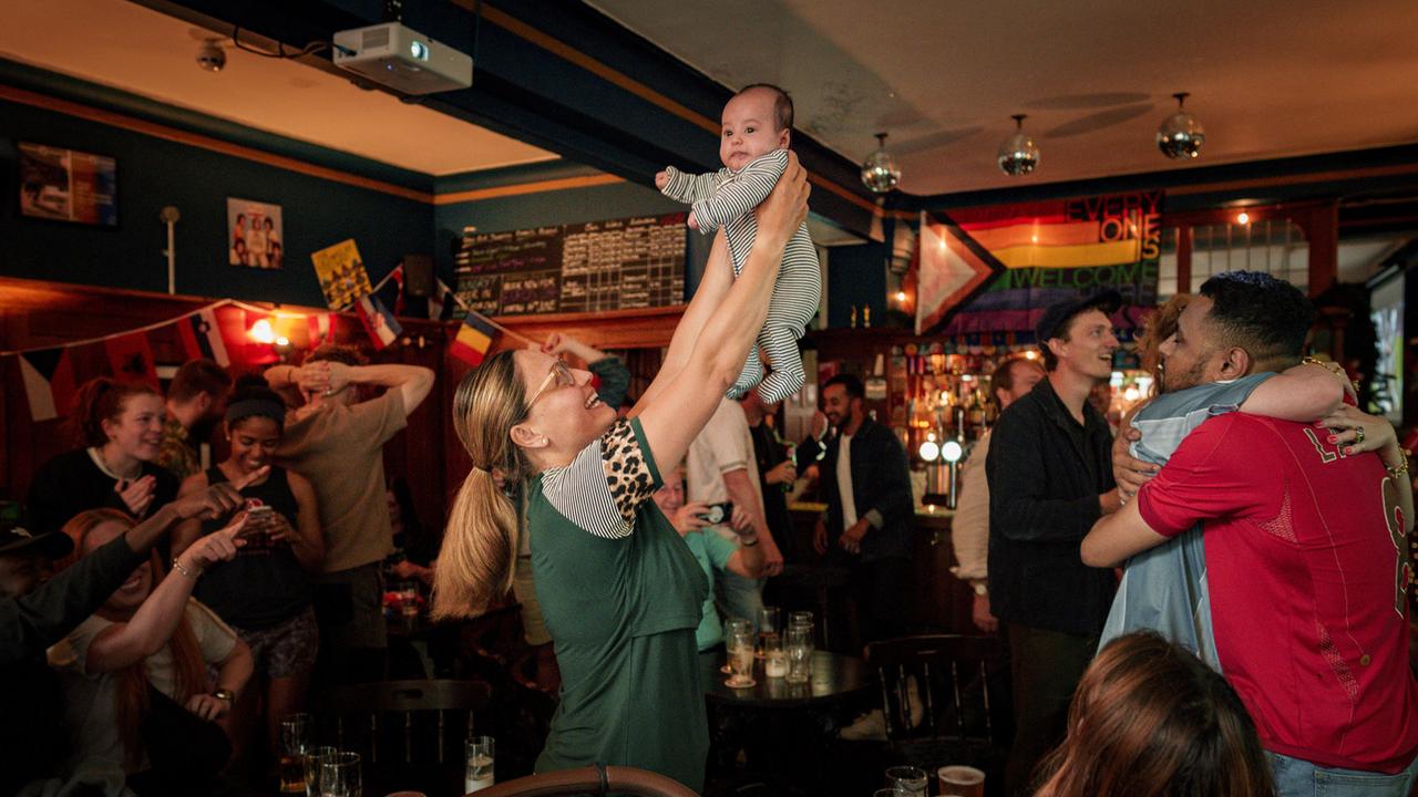 Dans un pub à Londres, une fan des "Three Lions" célèbre en soulevant un bébé un but de l'Angleterre contre la Slovaquie, en huitième de finale de l'Euro 2024, le 30 juin. [Keystone - AP Photo/Vadim Ghirda]