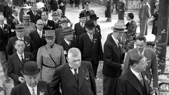 Le conseiller fédéral Walther Stampfli, devant 2e de. à gauche, et derrière lui en uniforme, le général Henri Guisan lors de la journée officielle à la foire de rassemblement de Bâle. [KEYSTONE/PHOTOPRESS-ARCHIV - ©Hans Gerber]