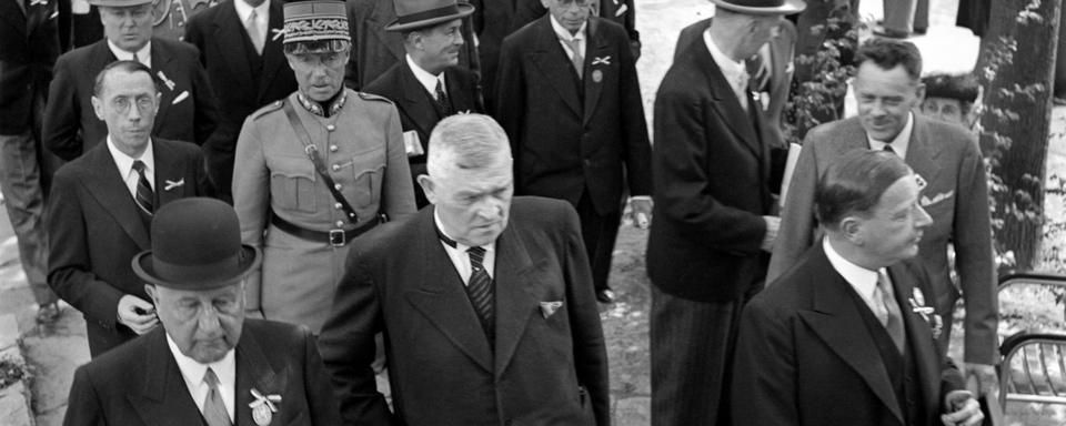 Le conseiller fédéral Walther Stampfli, devant 2e de. à gauche, et derrière lui en uniforme, le général Henri Guisan lors de la journée officielle à la foire de rassemblement de Bâle. [KEYSTONE/PHOTOPRESS-ARCHIV - ©Hans Gerber]