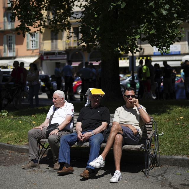 Trois personnes attendent le passage du Tour de France sur un banc à Pinerolo en Italie. [Keystone/AP Photo - Daniel Cole]