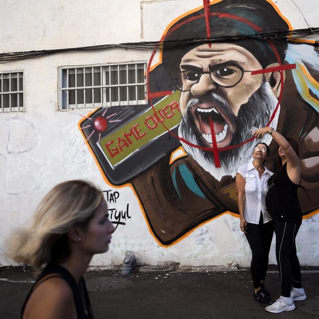 À Tel Aviv, deux femmes prennent un selfie à côté d'un graffiti du chef du Hezbollah libanais assassiné par Israël. [Keystone/AP Photo - Oded Balilty]