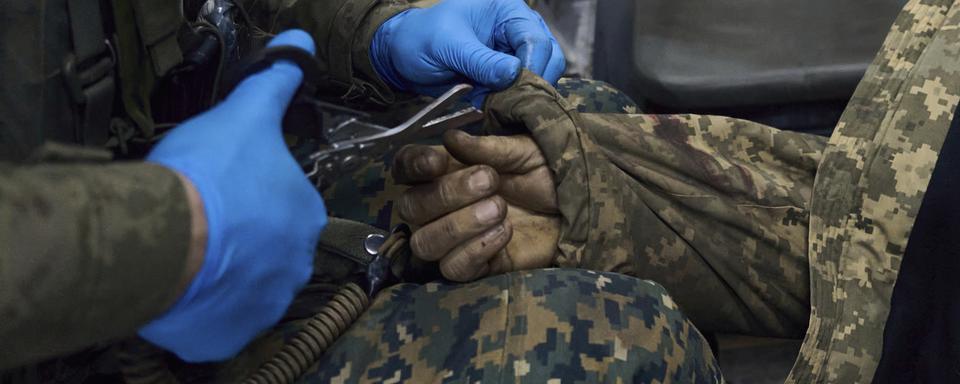 Un soldat infirmier donne les premiers soins à un blessé en Ukraine. [Keystone]