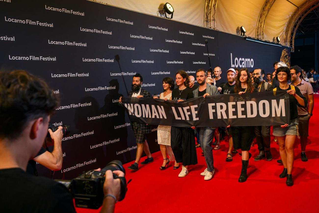 L'équipe du film "Mantagheye bohrani (Critical Zone)" du réalisateur iranien Ali Ahmadzadeh sur le  tapis rouge du Festival de Locarno avec une banderole "Femme, Vie, Liberté" le 12 août 2023. [KEYSTONE - JEAN-CHRISTOPHE BOTT]