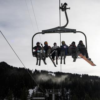 Des skieurs assis sur un télésiège de la station d'hiver de Villars dans les Alpes vaudoises. [Keystone - Jean-Christophe Bott]