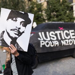 Une personne tient un portrait de Nzoy devant une banderole lors d'un rassemblement à la mémoire de Nzoy, tué par balle par un policier. [Keystone - Pierre Albouy]