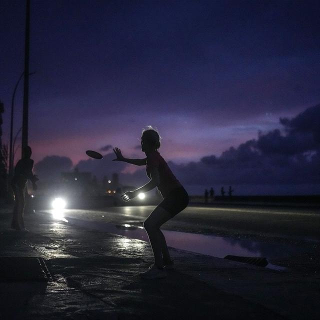 A woman prepares to catch a tossed frisbee during a massive blackout after a major power plant failed in Havana, Cuba, Friday, Oct. 18, 2024. [AP Photo/Keystone - Ramon Espinosa]