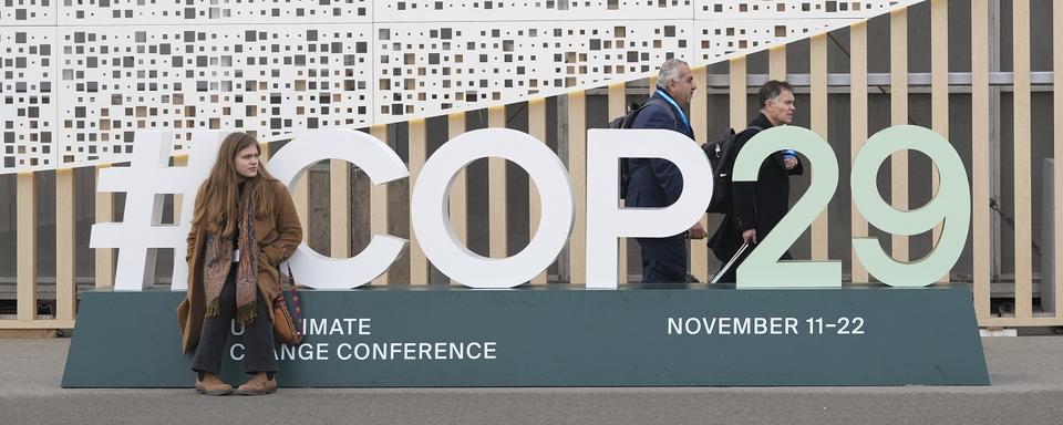 Des passants devant le signe du sommet mondial de la COP29 à Bakou, en Azerbaïdjan. [AP PHOTO/KEYSTONE - Sergei Grits]