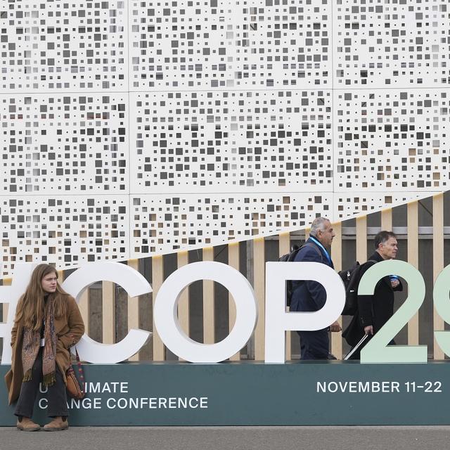 Des passants devant le signe du sommet mondial de la COP29 à Bakou, en Azerbaïdjan. [AP PHOTO/KEYSTONE - Sergei Grits]