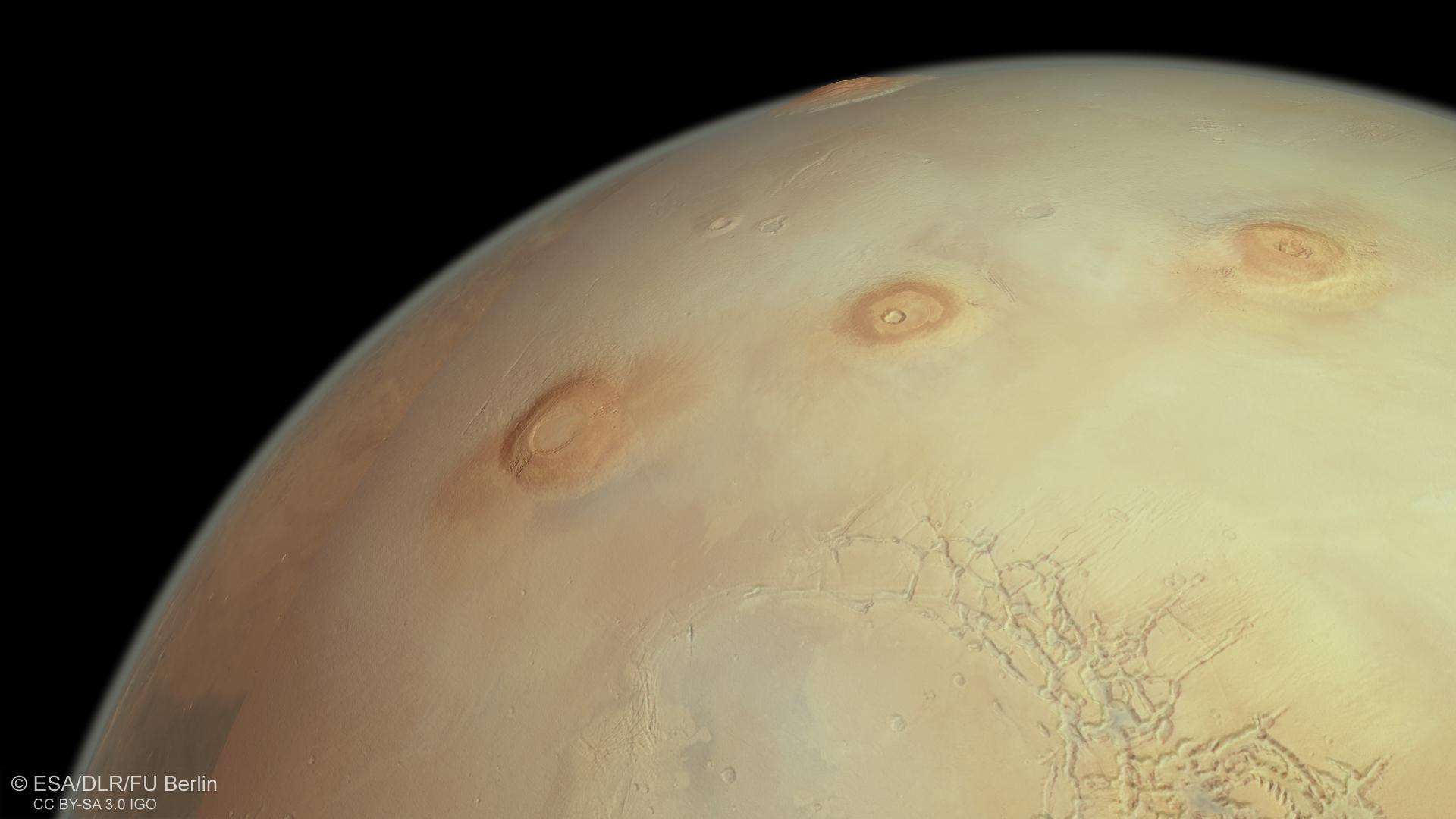 Au premier plan, trois volcans martiens: Arsia, Pavonis et Ascraeus Mons. Tout en haut de l'image, Olympus Mons, le plus haut volcan non seulement sur Mars, mais aussi dans tout le Système solaire, avec ses 26 kilomètres de haut. En bas à droite est visible le terrain fracturé de Noctis Labyrinthus, le "Labyrinthe de la nuit" de Mars. [Mars Express/ESA - Björn Schreiner/FU Berlin]