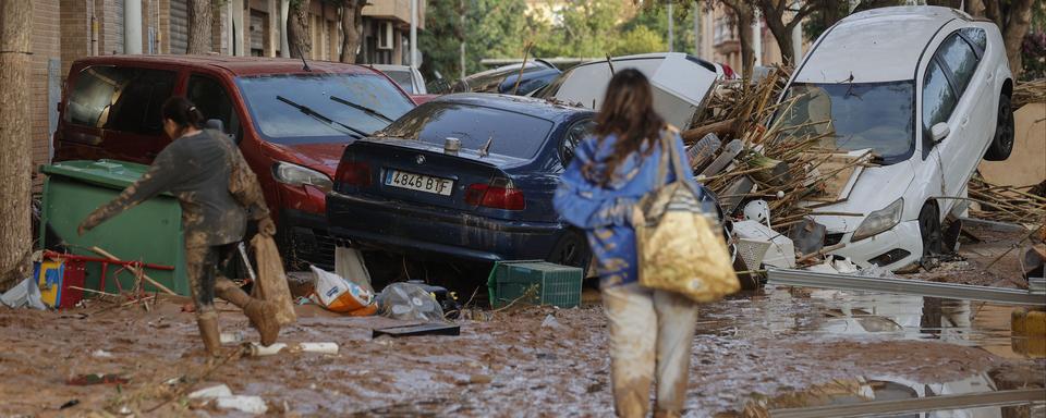 Des habitants marchent dans une rue couverte de boue à côté de voitures empilées après des inondations dans la municipalité de Paiporta, dans la province de Valence, en Espagne, le 30 octobre 2024. [Keystone - EPA/MANUEL BRUQUE]