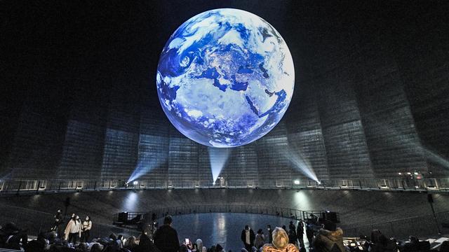 Sur cette photo du jeudi 7 octobre 2021, des visiteurs observent une installation terrestre géante lors de l'exposition "The Fragile Paradise" à l'intérieur de l'ancienne installation de stockage de gaz industriel "Gasometer" à Oberhausen, en Allemagne. [Keystone - AP Photo/Martin Meissner]