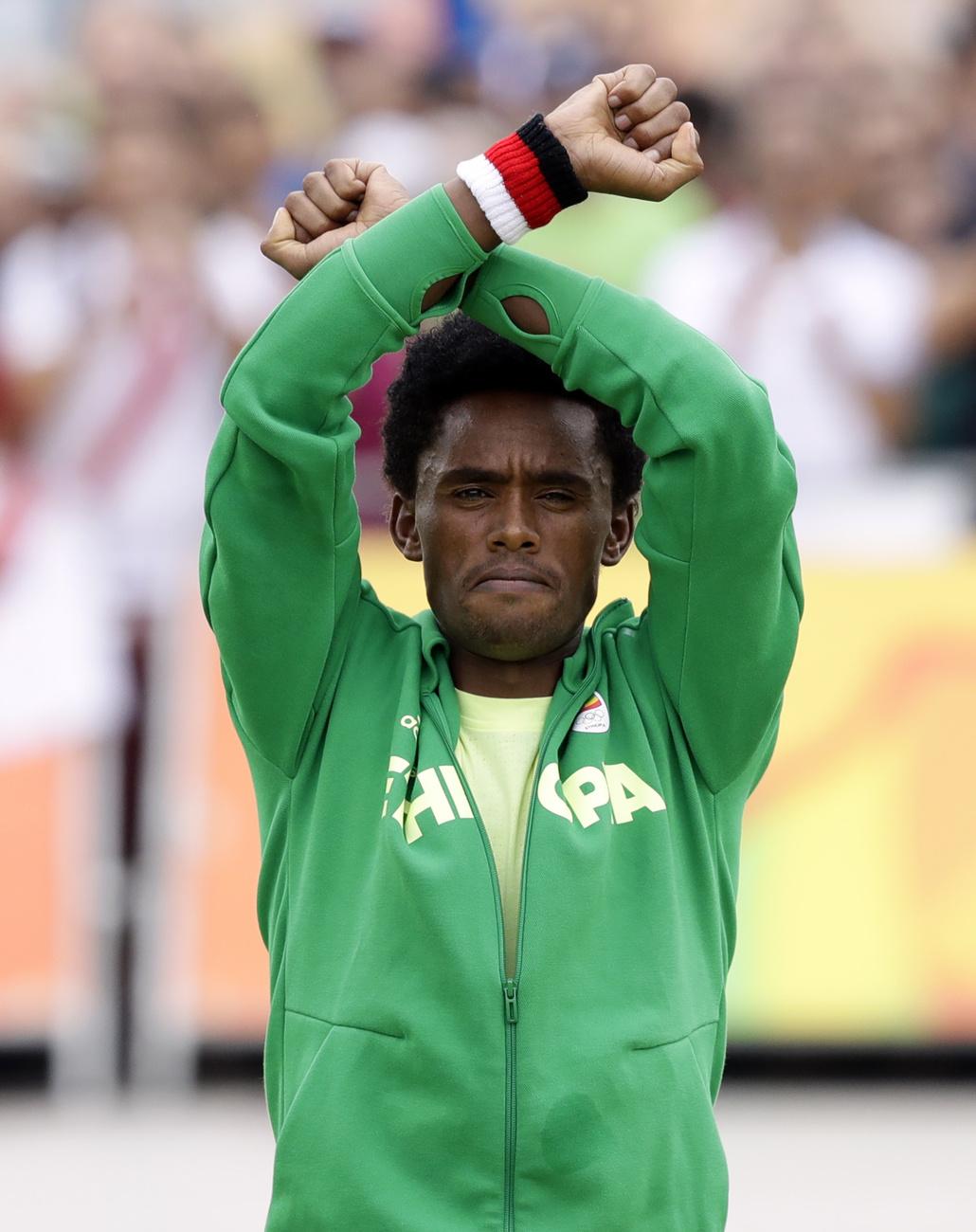 Le médaillé d'argent Feyisa Lilesa, originaire d'Éthiopie, lors d'une cérémonie de remise des prix alors qu'il croise les poignets pour tenter d'attirer l'attention du monde sur les récentes manifestations meurtrières dans sa région natale, Oromia, après le marathon masculin des Jeux olympiques d'été de 2016 à Rio de Janeiro, au Brésil, dimanche 21 août 2016. [KEYSTONE - ROBERT F. BUKATY]