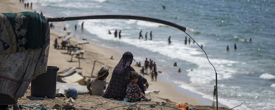 Une mère palestinienne et ses enfants déplacés regardent la mer depuis une plage à Gaza. [Abdel Kareem Hana - Keystone/AP Photo]