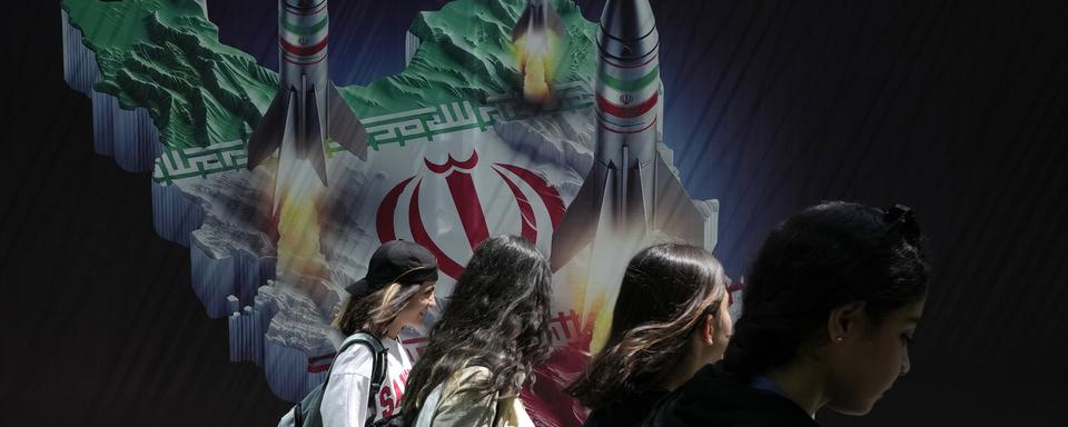 Des femmes iraniennes ne portant pas le foulard obligatoire, ou hijab, passent devant une banderole montrant des missiles lancés depuis la carte iranienne dans le nord de Téhéran, en Iran, le 19 avril 2024. [Keystone - AP Photo/Vahid Salemi]