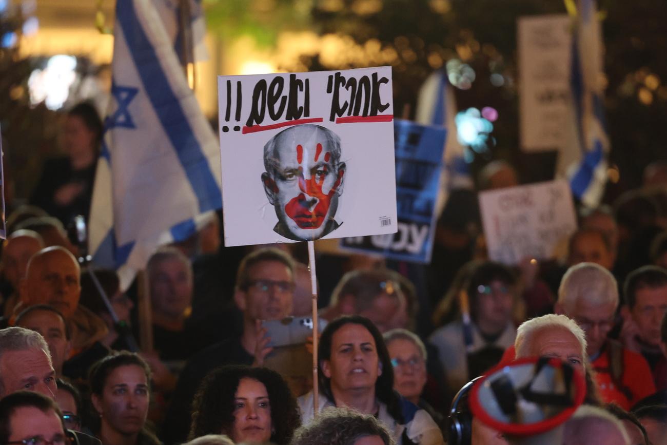 Une manifestante tient une pancarte représentant le Premier ministre Benjamin Netanyahu avec les mots "responsable" et "coupable" écrits en hébreu, lors d'une manifestation contre le gouvernement israélien sur la place Habima, à Tel Aviv. [KEYSTONE - ABIR SULTAN]