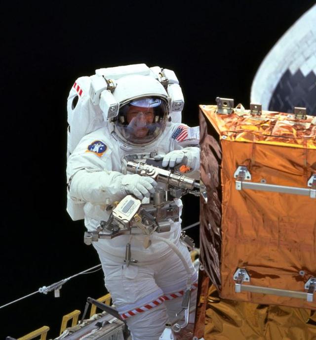 L'astronaute Claude Nicollier utilise l'outil Pistol Grip sur une enceinte de stockage, pendant la mission d'entretien 3A de Hubble en décembre 1999. [NASA]