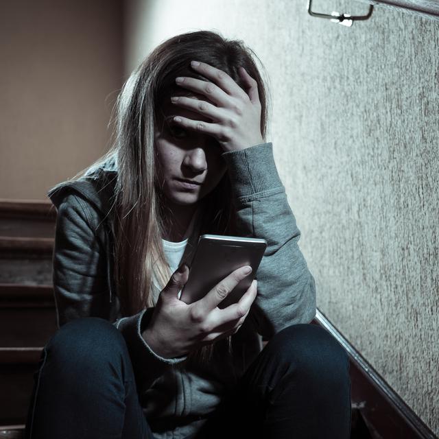 Une jeune fille victime de harcèlement regarde son téléphone avec désespoir. [Depositphotos - Sbartsmediagmail]