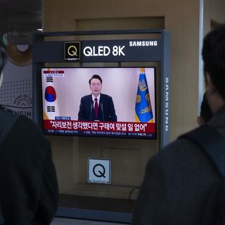 Des personnes regardent la retransmission en direct du président sud-coréen Yoon Suk Yeol s'adressant à la nation, dans une station de Séoul, en Corée du Sud, le 12 décembre 2024. [Keystone - JEON HEON-KYUN]