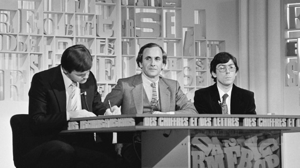 Le présentateur Patrice Laffont entouré de deux candidats durant la finale de l'émission "Des Chiffres et des Lettres" au Festival de télévision de Monte-Carlo, Monaco, le 6 février 1982. [AFP - Ralph Gatti]