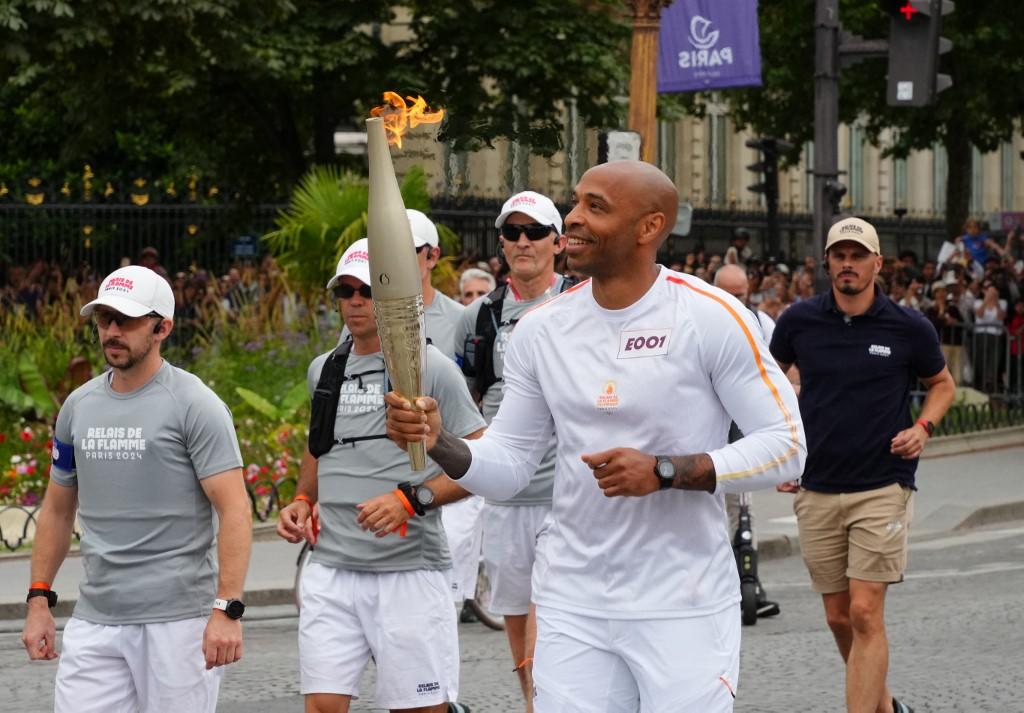 Thierry Henry court avec la flamme olympique sur les Champs-Elysées à Paris, lors de la fête nationale française, le 14 juillet 2024. [The Yomiuri Shimbun via AFP - RYOHEI MORIYA]