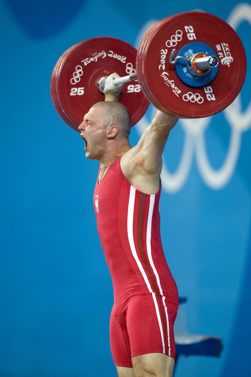 Le Polonais Szymon Kolecki lors de la séance d'épaulé-jeté de l'épreuve masculine d'haltérophilie pendant les Jeux Olympiques de Pékin de 2008, au gymnase de l'Université d'aéronautique et d'astronautique de Pékin, à Pékin, en Chine, le 17 août 2008. Kolecki a soulevé 179 kg et 226 kg avec un total de 403 kg pour remporter la médaille d'or. Il s'est aussi et surtout rasé la tête en soutien au peuple tibétain, opprimé par le Parti communiste chinois. [KEYSTONE - ALESSANDRO DELLA BELLA]