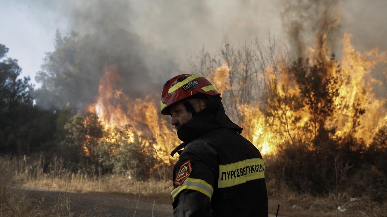 Un pompier se tient près d'un feu lors d'un incendie de forêt dans la zone résidentielle de Stamata près d'Athènes, en Grèce. [KEYSTONE - KOSTAS TSIRONIS]