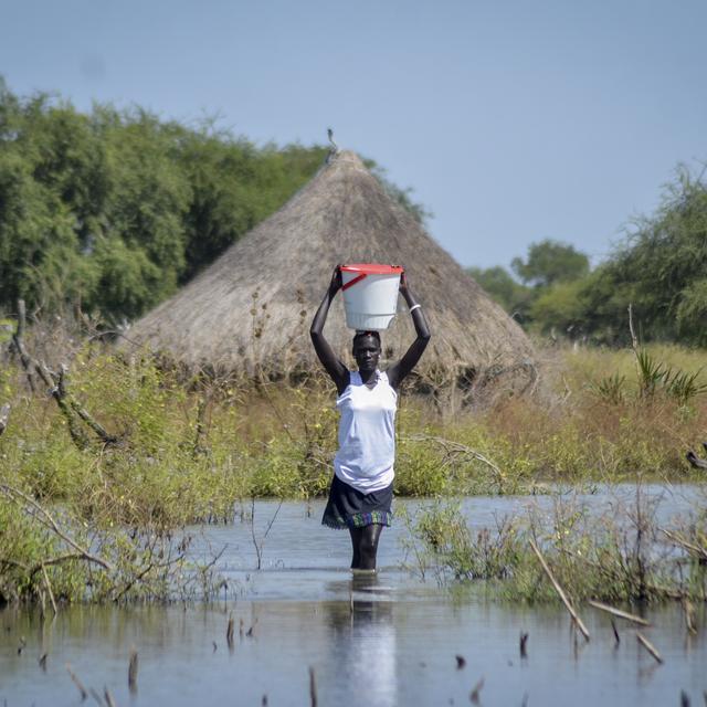 Une femme porte un seau sur la tête alors qu'elle patauge dans les eaux (archive). [Keystone - Maura Ajak]