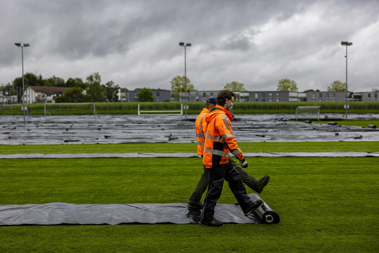 Des travailleurs bâchent un terrain de football à Kloten, le 7 mai 2024. [KEYSTONE - MICHAEL BUHOLZER]