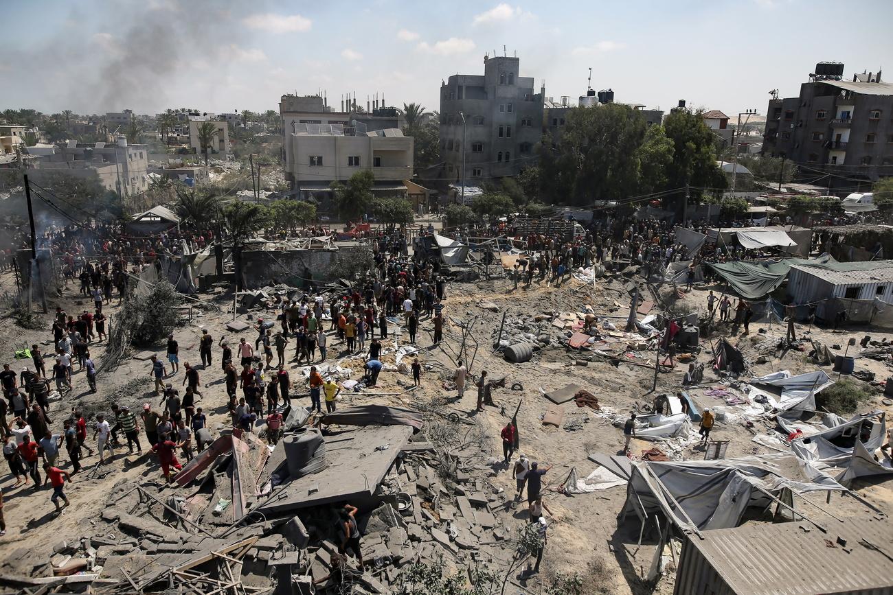 Des Palestiniens inspectent la scène après un raid israélien dans la zone d'Al-Mawasi, dans le sud de la bande de Gaza, le 13 juillet 2024. [KEYSTONE - HAITHAM IMAD]