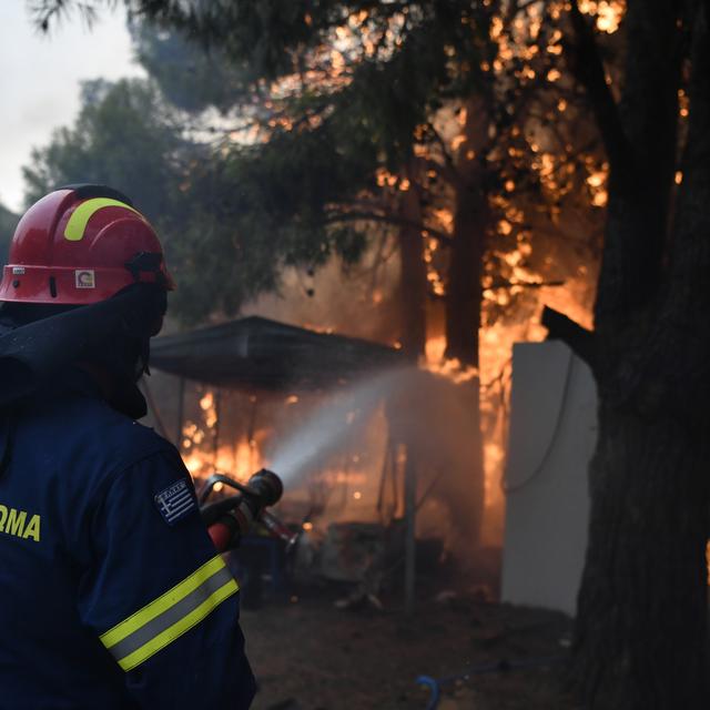 Un pompier grec se bat pour éteindre une maison en flamme au nord d'Athènes. La Grèce est touchée depuis plusieurs jours par des mégas incendies. Le 12 août 2024. [AP Photo/KEYSTONE - Michael Varaklas]