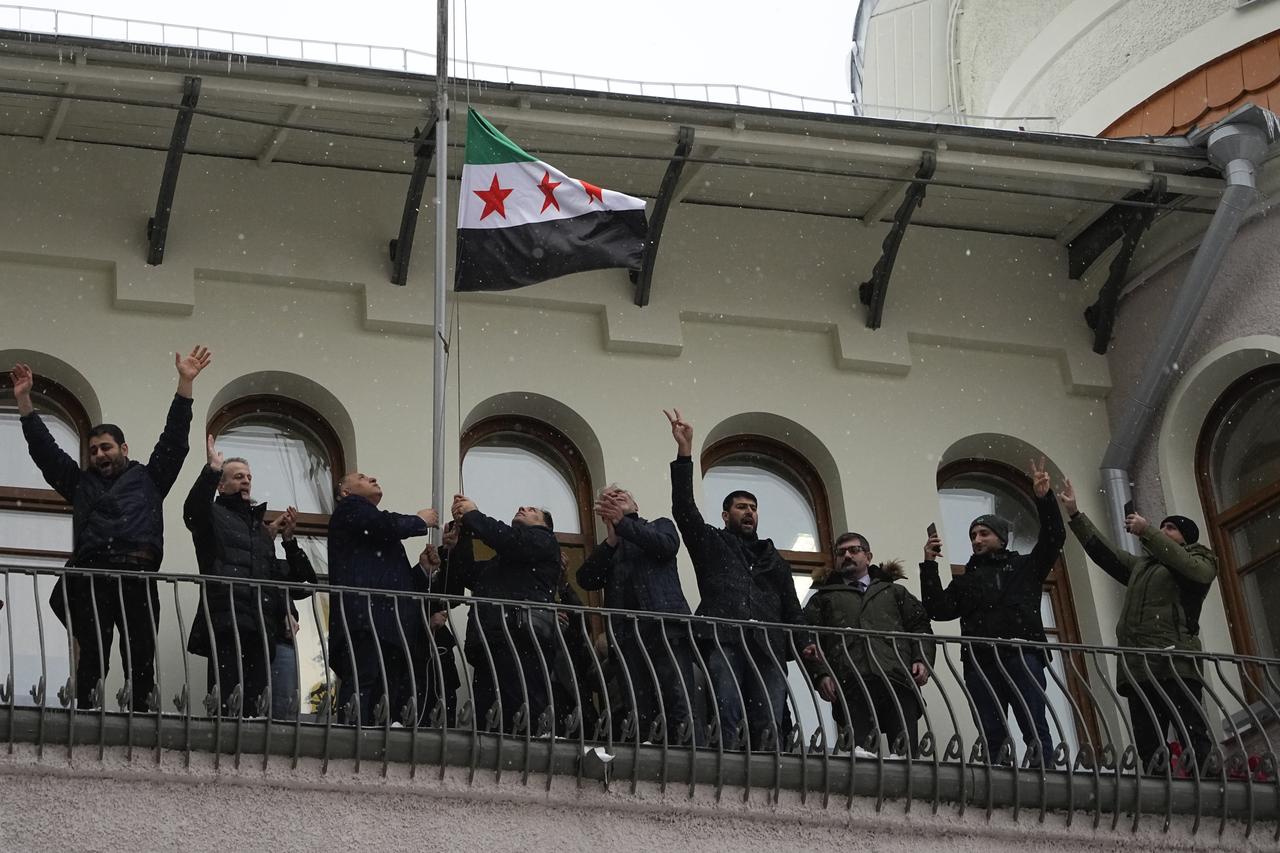 Un groupe d'hommes hisse le drapeau de l'opposition syrienne sur l'ambassade de Syrie à Moscou, en Russie, lundi 9 décembre 2024. [KEYSTONE - ALEXANDER ZEMLIANICHENKO]