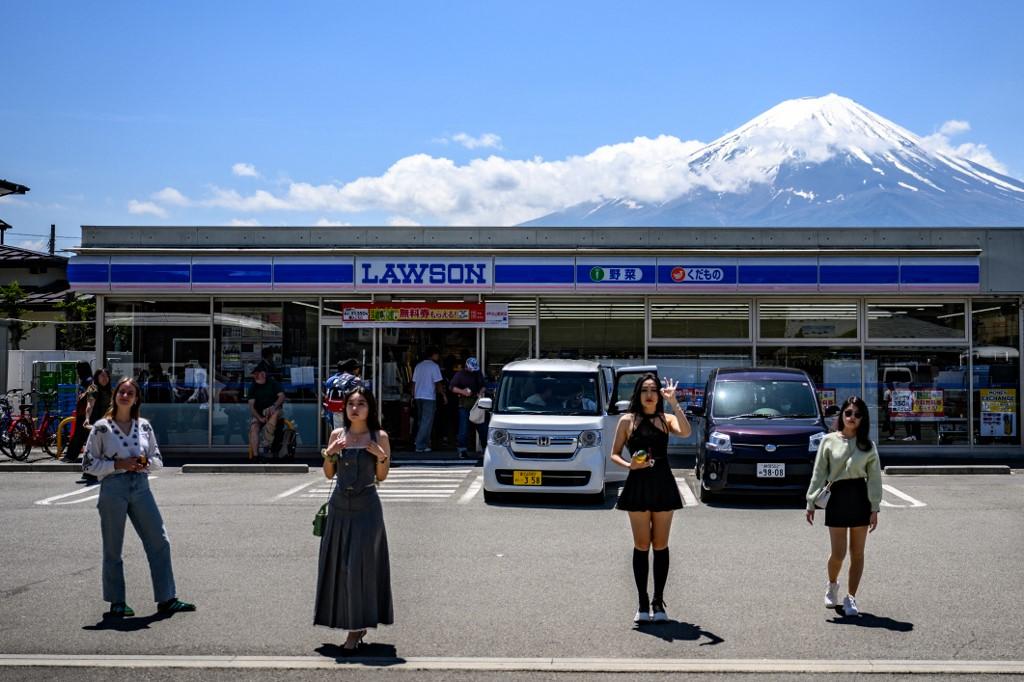 Des touristes posent devant une supérette japonaise "Lawson" avec le mont Fuji en arrière-plan. [AFP - PHILIP FONG]