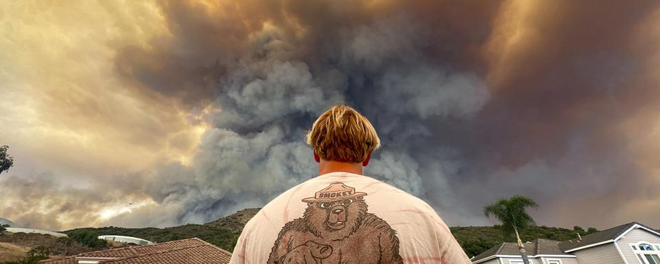 Un homme regarde la fumée liée à l'Airport Fire s'élever derrière Meander Lane, à Trabuco Canyon, en Californie. [Keystone]