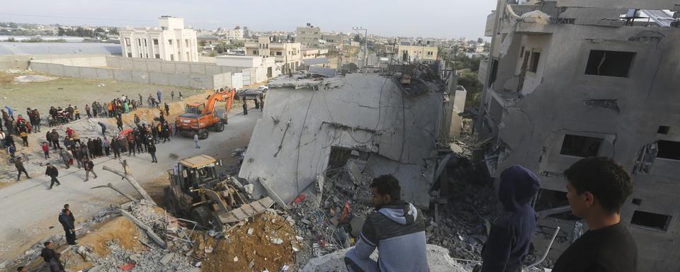 Des palestiniens observant la destruction d'un immeuble de Rafah par l'armée israélienne. [Keystone/AP Photo - Hatem Ali]