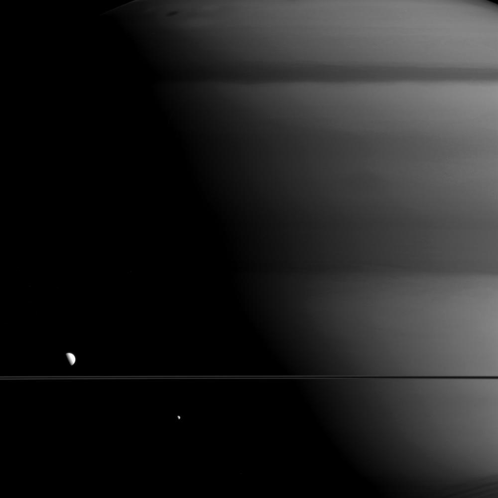 Bien que suffisamment grandes pour être visibles, les lunes Mimas (à droite, 396 km de diamètre) et Dioné (à gauche, 1123 km de diamètre) sont minuscules comparées à Saturne (120'700 km de diamètre). Image prise avec la caméra grand angle de la sonde Cassini le 27 mai 2015. [NASA - JPL-Caltech/Space Science Institute]