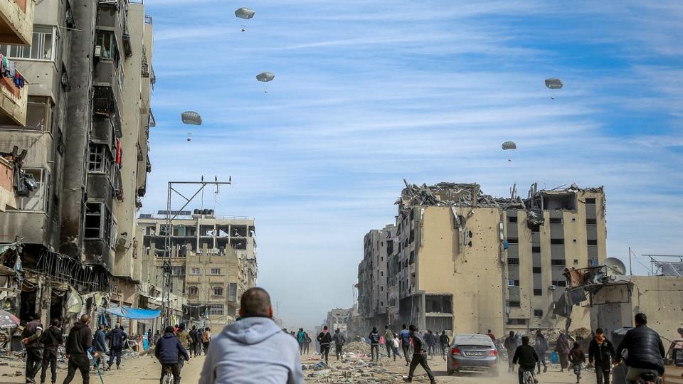 Des Palestiniens courent le long d'une rue alors que de l'aide humanitaire est larguée dans la ville de Gaza le 1er mars 2024. [AFP - -]