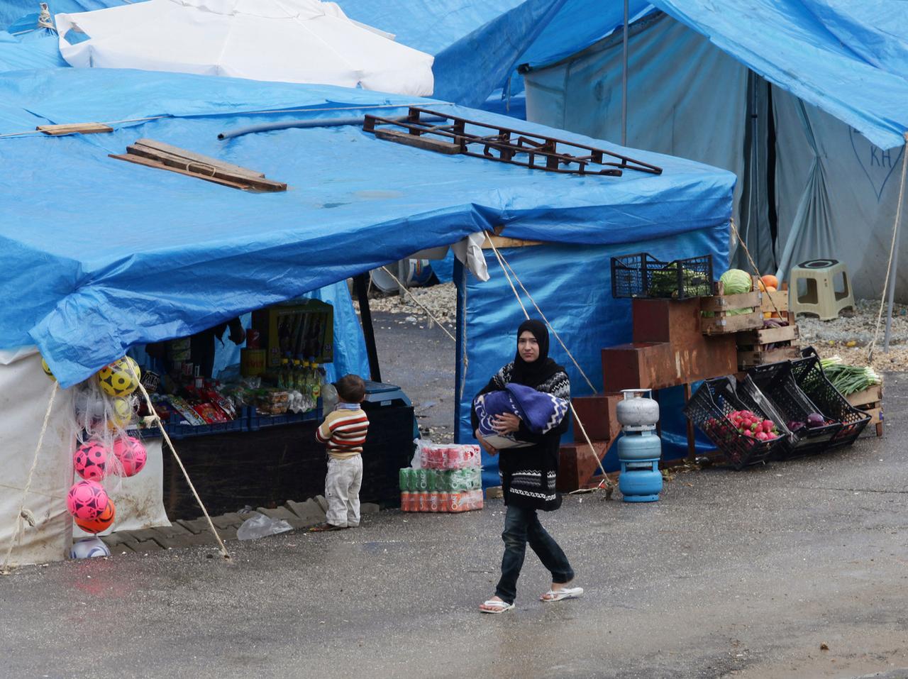 Une femme portant un bébé marche devant un stand de nourriture dans le camp de réfugiés de Yayladagi, à la frontière avec la Syrie, le 14 mars 2012. L'immigration syrienne pourrait contribuer à pallier le déclin de la natalité en Turquie, mais le sujet n'est pas discuté publiquement. [KEYSTONE - BURHAN OZBILICI]