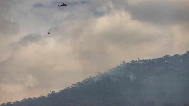 Les pompiers australiens tentent vendredi de maîtriser un immense feu de brousse se propageant à travers un parc national du sud-est du pays. [Keystone - Diego Fedele]