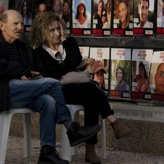 Un couple assis devant des photographies d'otages israéliens à Tel Aviv, après l'annonce de la confirmation du cessez-le-feu par Benjamin Netanyahu. 17 janvier 2025. [AP Photo/Keystone - Maya Alleruzzo]