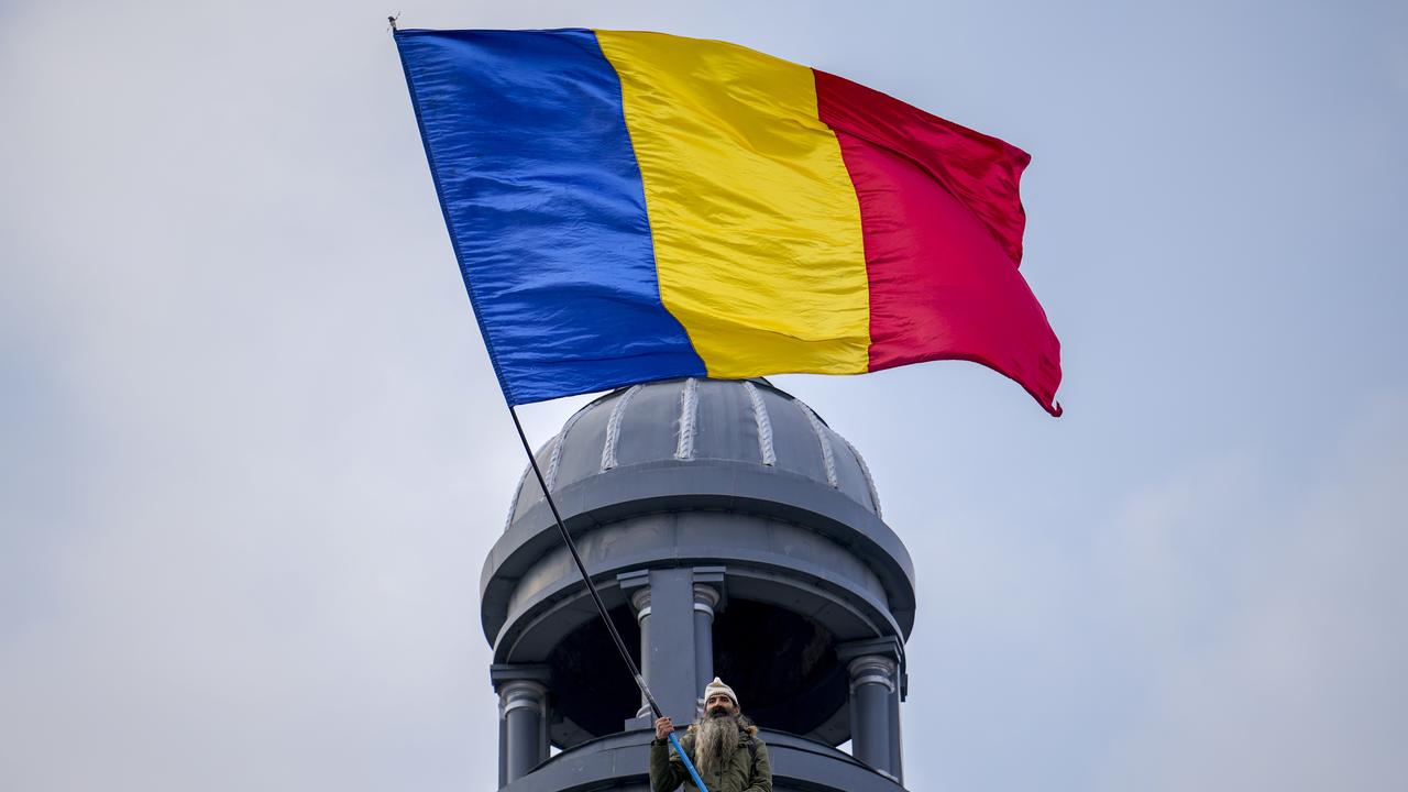 Un homme perché sur le toit d'un immeuble agite le drapeau roumain lors d'un rassemblement organisé par l'Alliance pour l'unité des Roumains (AUR), un parti d'extrême droite, appelant à des élections libres [Keystone]