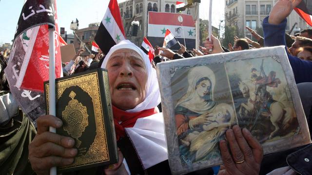 Une femme syrienne tient un Coran et des icônes chrétiennes durant une manifestation à Damas, le 28 novembre 2011. [Louai Beshara]