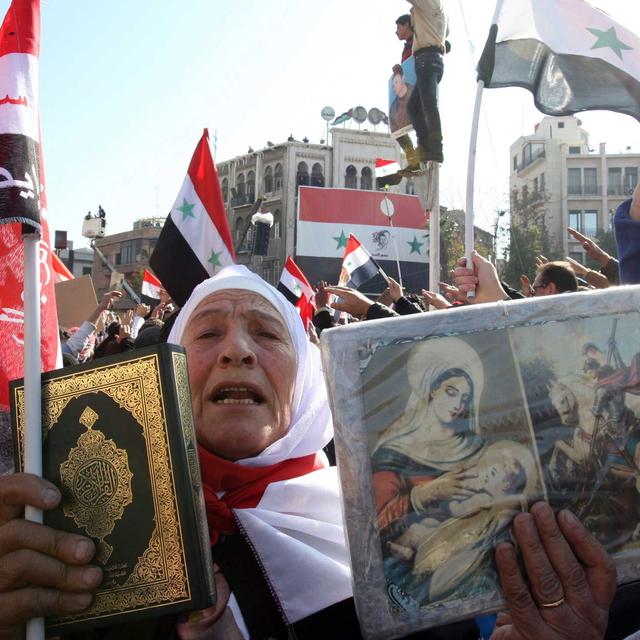 Une femme syrienne tient un Coran et des icônes chrétiennes durant une manifestation à Damas, le 28 novembre 2011. [Louai Beshara]