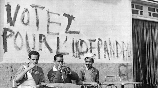 Des Algériens prennent leur café sous une inscription appelant à voter lors du référendum pour l'indépendance de l'Algérie, le 17 juin 1962 à Alger.