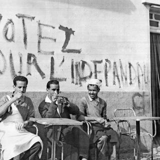 Des Algériens prennent leur café sous une inscription appelant à voter lors du référendum pour l'indépendance de l'Algérie, le 17 juin 1962 à Alger.