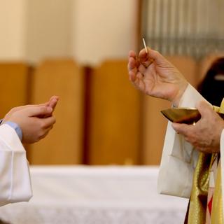 Main de l'évêque qui dispense la Sainte Eucharistie pendant la communion. [Depositphotos - ChiccoDodiFC]