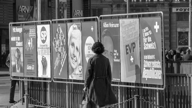 Les élections fédérales et régionales de 1971 en Suisse ont la particularité de permettre pour la première fois à environ deux millions de femmes d'exercer leur droit de vote. À Zurich, une femme passe devant un panneau d'affichage sur lequel divers partis politiques font connaître leur programme à l'approche des élections du 19 octobre 1971. [KEYSTONE/PHOTOPRESSE-ARCHIVE/FW]