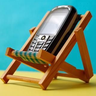 Utiliser son téléphone portable durant les vacances à l'étranger peut coûter cher. Natel, chaise longue, vacances [miqul]