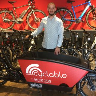 Romain Marandet, patron de la boutique Cyclable, aux côtés d'un modèle de vélo cargo électrique. [RTS - Jérôme Zimmermann]