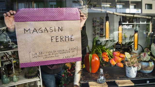 Un fleuriste pose une affiche pour annoncer la fermeture temporaire de son magasin de fleurs suite a la fermeture des magasins dans le canton de Vaud le lundi 16 mars 2020 a Lausanne. Le gouvernement vaudois a decide lundi de prendre de nouvelles mesures exceptionnelles pour proteger la population contre le coronavirus (Covid-19). L'arrete interdit l'exploitation des lieux de commerce, sauf les commerces d'alimentation ou de premiere necessite. [KEYSTONE - Jean-Christophe Bott]